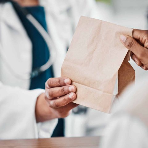 Pharmacy, medication and pharmacist giving bag to a patient for treatment, cure or remedy. Healthcare, people and woman with a brown paper package from a chemist for medicine in a drugstore or clinic.
